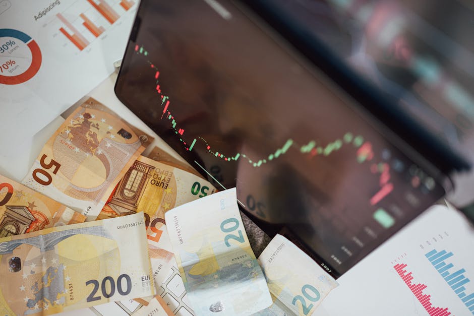 A black handheld magnifying glass positioned over a scientific calculator, highlighting a stack of 50 euro banknotes underneath the glass. The calculator is situated on a surface with a partially visi